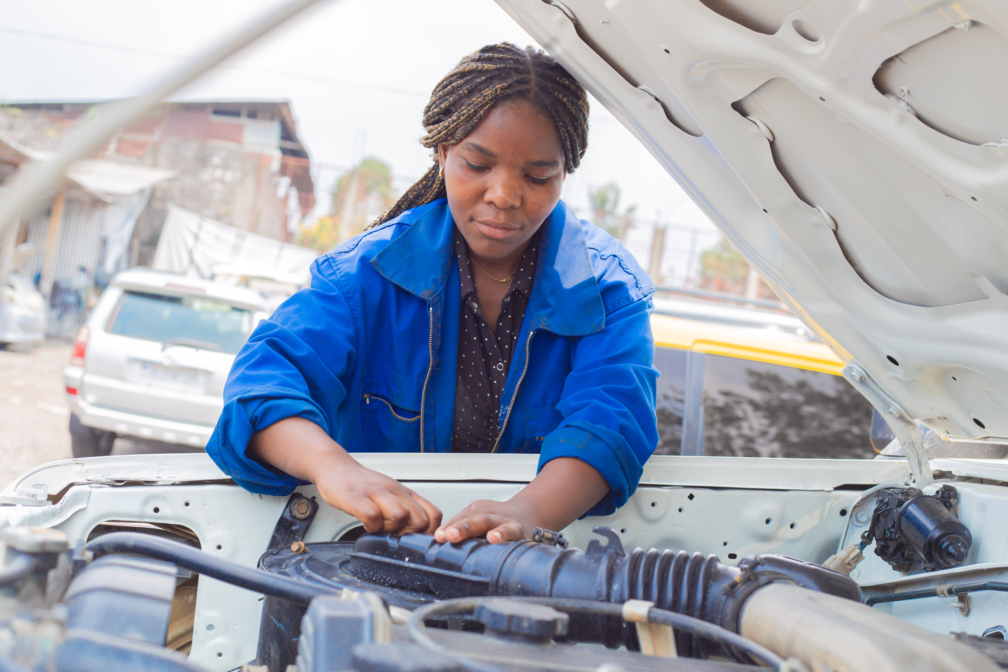 Girl leaning over the open hood of a car, herhands are working on teh engine.
